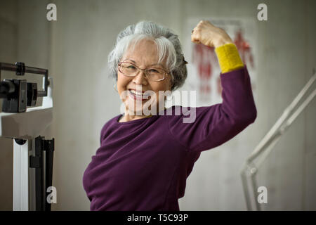 Smiling senior woman flexing her muscles while standing on scales. Stock Photo