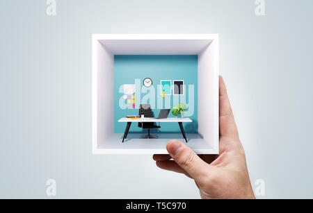 A businessman holding up a miniature square office in his hand. Portable co-working work space business concept. Mixed media image. Stock Photo