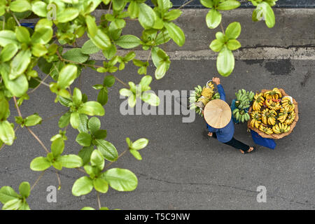 Person in asian bamboo hat walking with bananas on bike outdoors Stock Photo