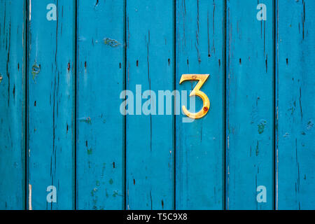 Brass Number 3 on a teal coloured wooden garden gate. UK Stock Photo