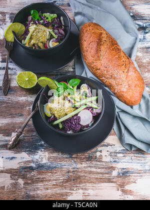 Italian ciabatta and fresh vegetable salad in a dark bowl. Salad with radish, red cabbage, cucumber, pesto and sesame seeds. Stock Photo