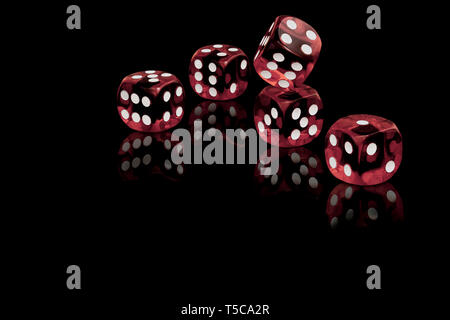Five red dices isolated on a black background casting a reflection on the surface. Stock Photo