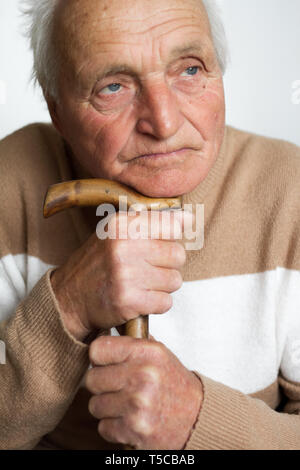 Portrait of an old sad man who put his head on the handle of a wooden cane, the concept of loneliness at home. Stock Photo