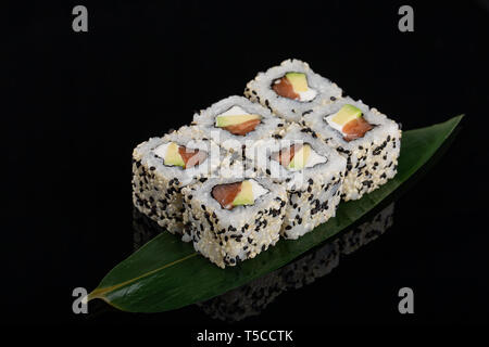 Uramaki maki sushi, two rolls on banana leag at black background. Philadelphia cheese, tuna, cucumber and sesame Stock Photo