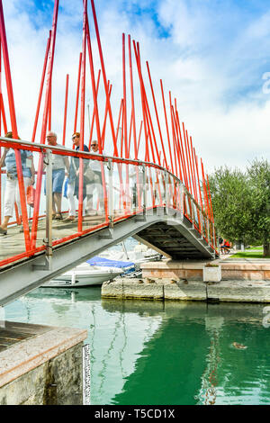 BARDOLINO, LAKE GARDA, ITALY - SEPTEMBER 2018: People walking across the footbridge over the entrance to the small harbour in Bardolino on Lake Garda. Stock Photo