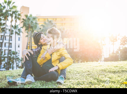 Happy gay couple hugging and laughing together sitting on grass in a park - Young women lesbians having a tender moment outdoor Stock Photo