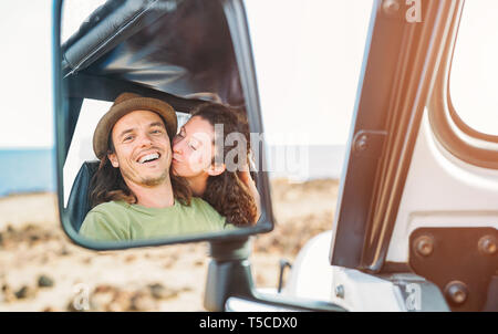 Happy couple having a tender moment during their road trip with a convertible car - Pov in a car mirror of young travel people in their vacation Stock Photo