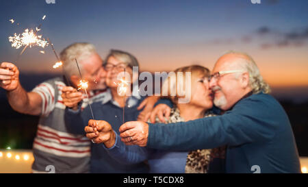 Happy senior friends celebrating with sparklers outdoor - Older people having a fun and tender moment on rooftop Stock Photo