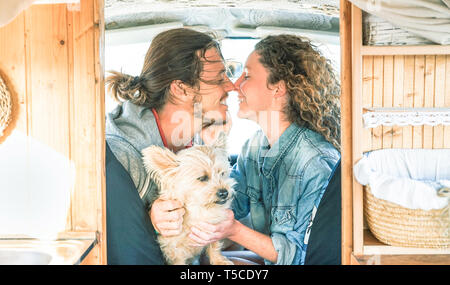 Happy couple close to kiss inside a vintage minivan with their dog during a road trip - Young people having a tender moment in vacation holidays Stock Photo