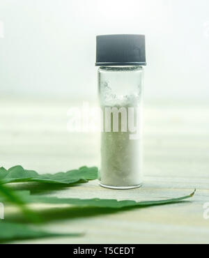 CBD Cannabidiol crystals isolate in glass container with Cannabis leaf on table Stock Photo