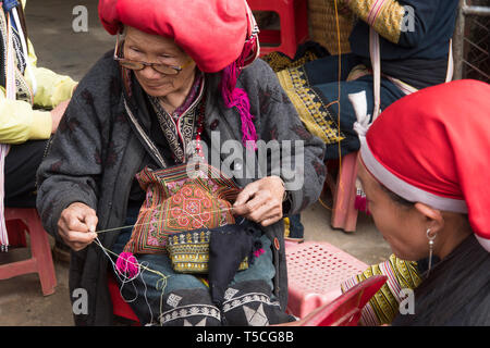 Red dzao ethnic minority woman sewing in Sa Pa, Lao Cai province, Vietnam. elderly woman makes souvenirs on the street. TA PHIN, LAO CAI, VIETNAM - 12 Stock Photo