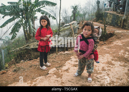 TA PHIN, LAO CAI, VIETNAM - 12 January 2019: A small child in a bag behind a child girl. Red dzao - a small nation of North Vietnam Stock Photo