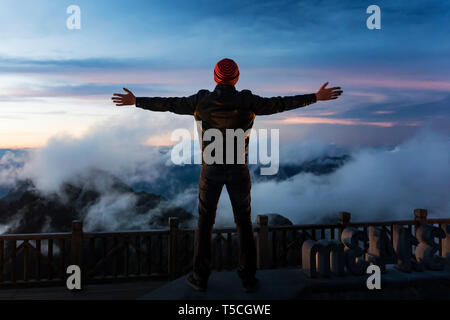 Silhouette of man is standing on top of mountain and spreading hand before sunrise. Sunset on Fansipan, Emotional scene. Freedom travel adventure and  Stock Photo