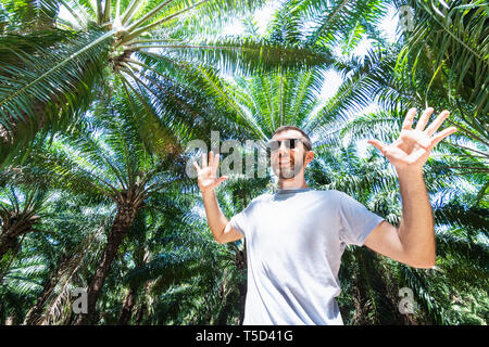 Bearded smiling man with glasses standing in the palm tree forest. Stock Photo