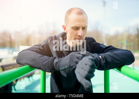 Photo of young athlete looking at watch while pulling up on green horizontal bar Stock Photo