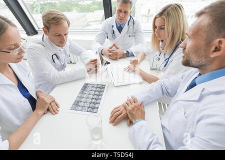 Team of doctors discuss brain scan sitting around the table Stock Photo