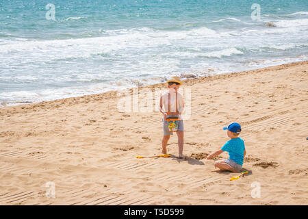 two young boys play with bucket and spades on a sandy beach in Alicante Spain Stock Photo