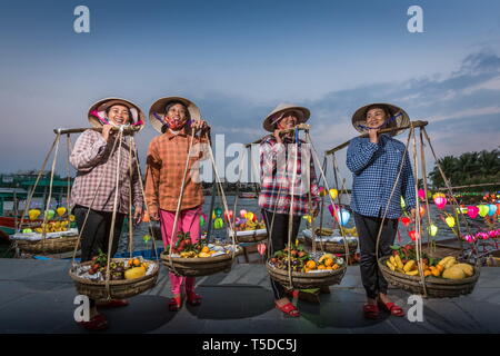 Hoi An, Vietnam - February 21 2019: Vietnamese women, fruits vendors wearing traditional conical hats and shoulder carrying pole in Hoi AN