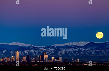 The worm moon sets behind the Rocky Mountains above the Denver skyline. Stock Photo