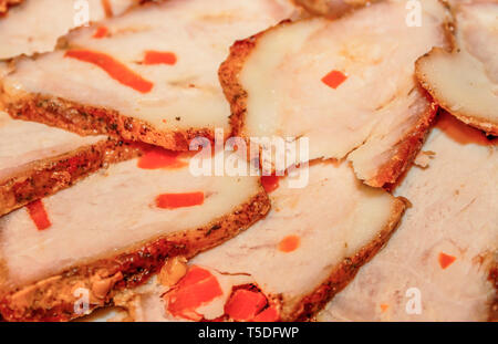 Sliced baked ham, stuffed with carrots and spiced spread out on a plate close up as background Stock Photo