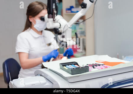 Young female dentist treating root canals using microscope at the dental clinic. Young man patient lying on dentist chair with open mouth. Dentist Stock Photo