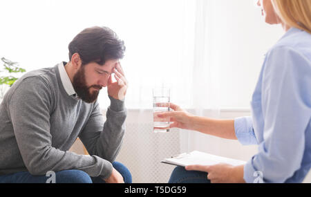 Psychoanalyst offering glass of water to depressed male patient Stock Photo