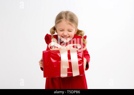 Portrait of little girl in red dress on isolated white background. Smiling Girl in shirt with gifts in hands looking at camera. Isolated gray backgrou Stock Photo