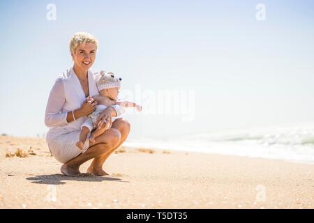 Happy blond mother with 4 months old baby boy on the beach, Portugal Stock Photo