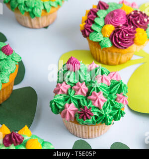 Brightly and creatively decorated cupcakes with succulents and flowers on a bright blue background with paper tropical leaves Stock Photo