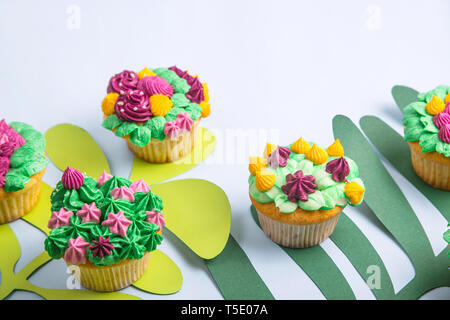 Brightly and creatively decorated cupcakes with succulents and flowers on a bright blue background with paper tropical leaves. Top view, flat lay Stock Photo
