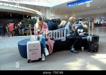 People women travellers sitting waiting flight Bristol airport departure lounge bench with luggage looking at mobile phone 2019 UK  KATHY DEWITT Stock Photo