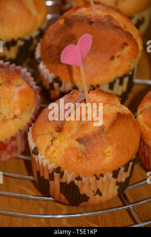 close up view of homemade sweet and golden baked muffins, homemade muffins with cracks on cooling metal grid on wooden table with love decoration Stock Photo