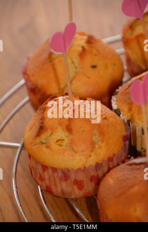 homemade muffins with cracks on cooling metal grid on wooden table with love decoration, macro of homemade sweet and golden baked muffins Stock Photo