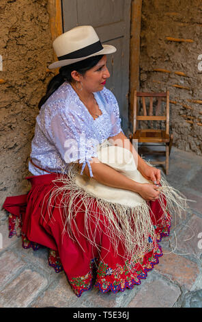 Indigenous Chola Cuencana woman in traditional clothing showing the weaving technique of Panama hat, Unesco Intangible heritage of Cuenca, Ecuador. Stock Photo