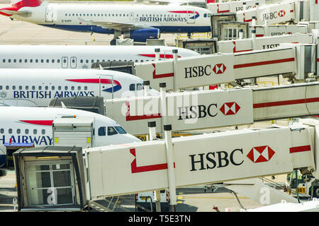LONDON GATWICK AIRPORT, ENGLAND - APRIL 2019: British Airways planes linked up to passenger air bridges carrying HSBC signs at Gatwick Airport's South Stock Photo
