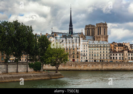 View of Seine river and spire of famous Notre-Dame de Paris cathedral among typical parisian buildings under cloudy sky. Stock Photo