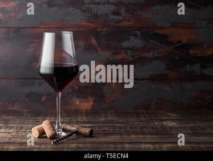 Elegant glass of red wine with corks and corkscrew on dark wooden background. Stock Photo