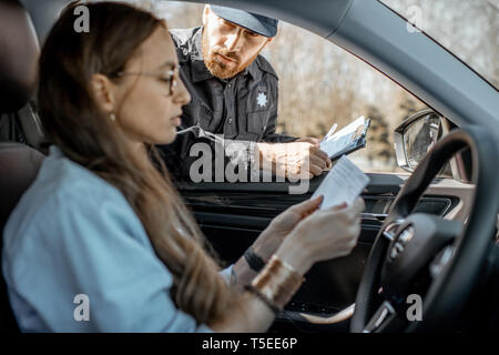 Policeman checking documents of a young female driver sitting in the car, view from the car interior Stock Photo