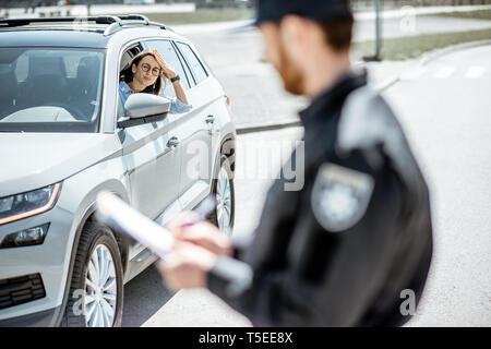 Upset female driver sitting in the car with policeman issuing a fine on the roadside Stock Photo