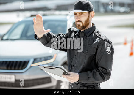 Portrait of a handsome policeman in uniform standing in front of a car on the roadside Stock Photo