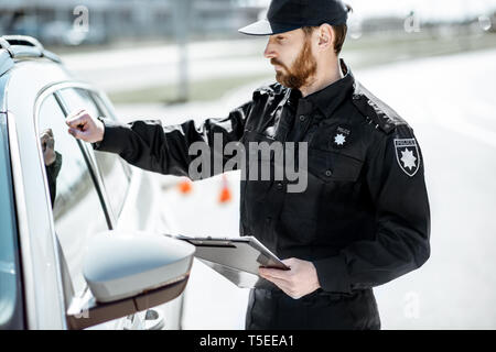 Policeman knocking at the window to a car driver, stopping the car for the offense Stock Photo