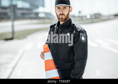 Portrait of a policeman in uniform standing with traffic cones on the city road Stock Photo