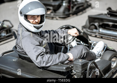 Portrait of a male racer in sportswear and protecive helmet sitting in the go-kart on the track outdoors Stock Photo