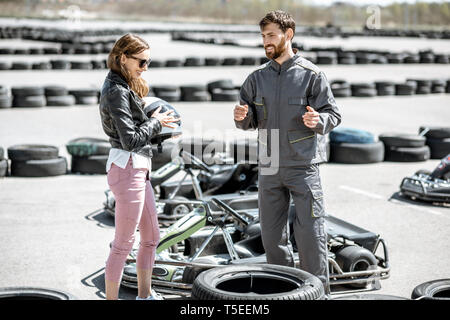 Male instructor in sportswear talking with young woman driver standing on the track with go-karts outdoors Stock Photo