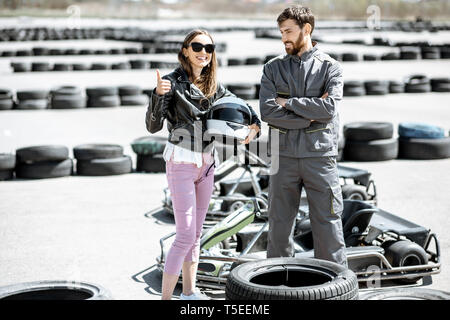 Happy instructor in sportswear with young woman driver on the go-kart track outdoors Stock Photo