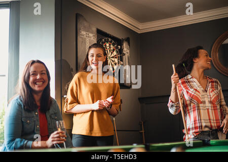 Small group of female friends playing a game of pool in a games room in a house. Stock Photo