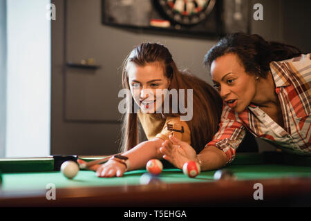 Close-up of two female friends playing a game of pool. They are lining up the shot and practicing. Stock Photo