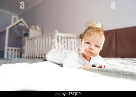 A newborn baby is lying on his stomach in the nursery on the bed. Kid with funny chubchik on his head Stock Photo