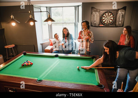 Small group of friends playing pool in a games room in a house. Stock Photo