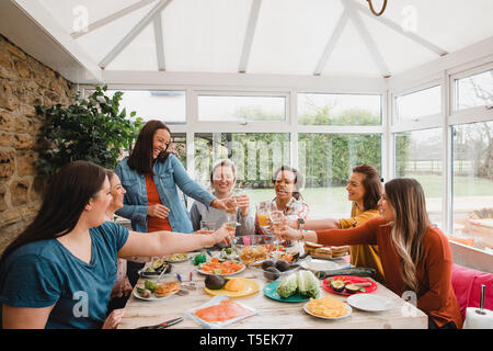 Small group of friends making a celebratory toast while sitting around a table in a conservatory. Stock Photo